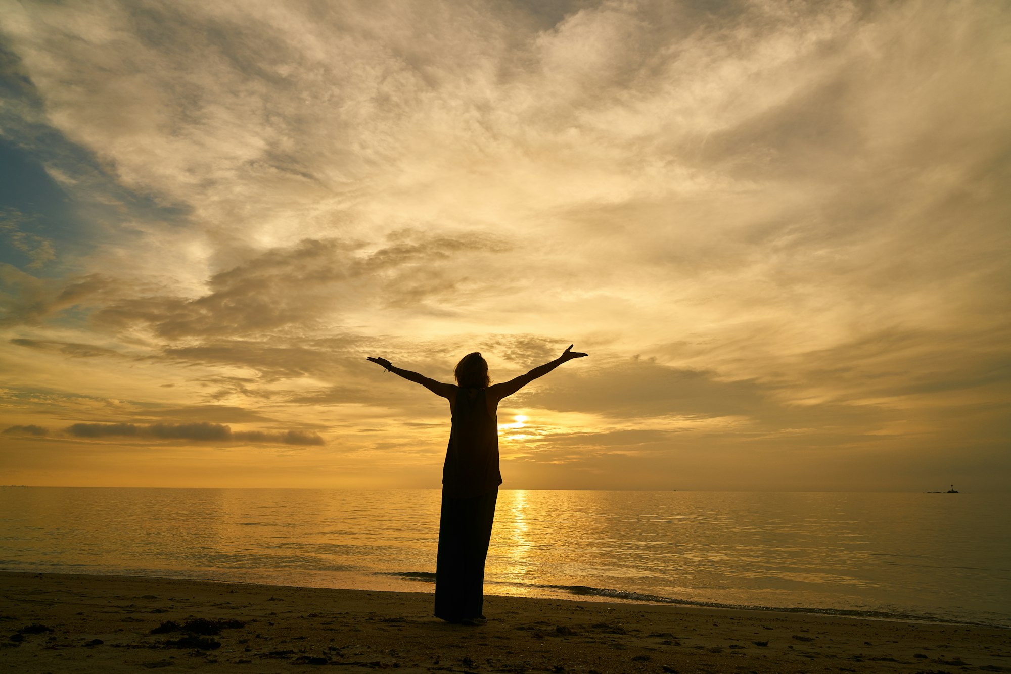 A person greeting the sunrise on a beach with arms raised